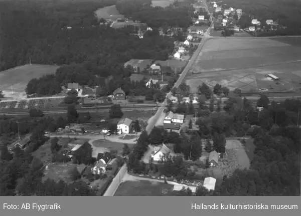 Flygfoto över Skreanäs som genomskärs av järnvägen mellan Falkenberg-Halmstad. Skogssprängt odlingslandskap med gårdar och villabebyggelse. Bilden har använts till vykort.
