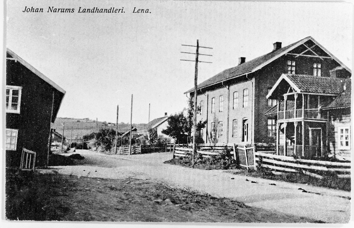 Parti fra Lena ca. 1910. På bildet står det skrevet Johan Narums Landhandleri, som er den store teglsteinsbygningen til høyre i bildet. Huset med veranda i høyre bildekant tilhørte Johan Grindstad som var smed. Raubua, som var lagerbygg tilhørende nedre Valle, skimtes i venstre bildekant.
Bildeet er i sin opprinnelse et prospektkort i farger, og det er også merket Eneret S.K.F.