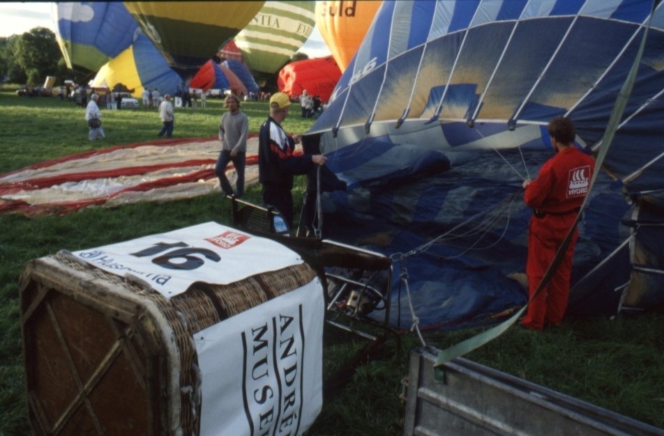 Två personer håller i ballonghöljet till en blåluftballong. Ballongkorgen har siffran16 och en dekal för "Andréemuseet".