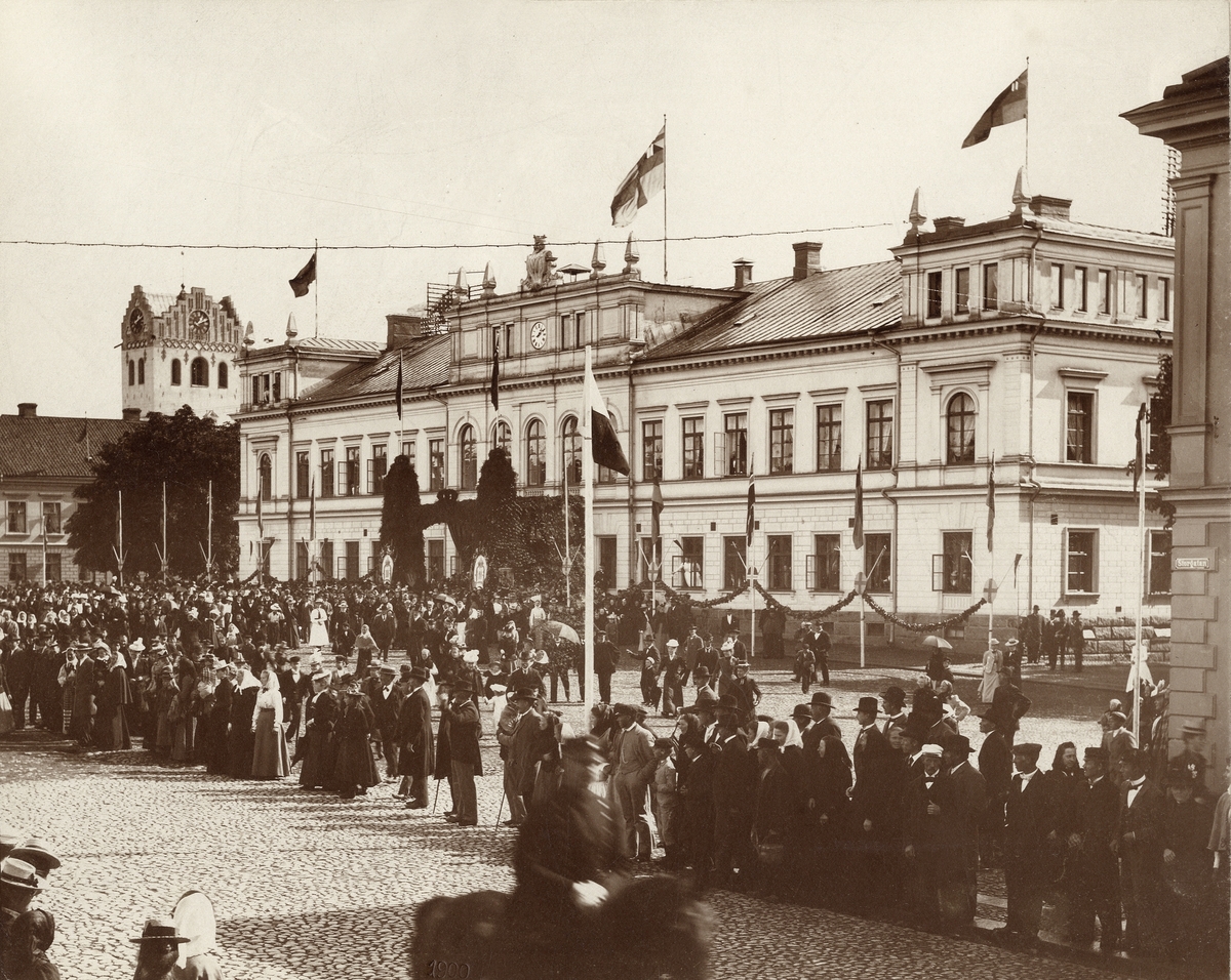Kung Oscar II på besök i Växjö, 4 september 1900. 
Folk står och väntar på kungen i korsningen Kungsgatan/Storgatan med stadshuset/stadshotellet till höger och dåv. domkyrkans torn i bakgrunden.