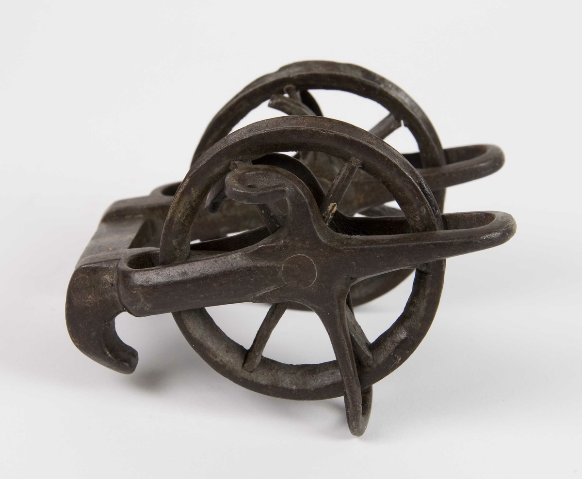 Armbrøstspenner av jern. To løpehjul i jern montert på en skaling med bro med to påsmidde haker for feste av buesnor.