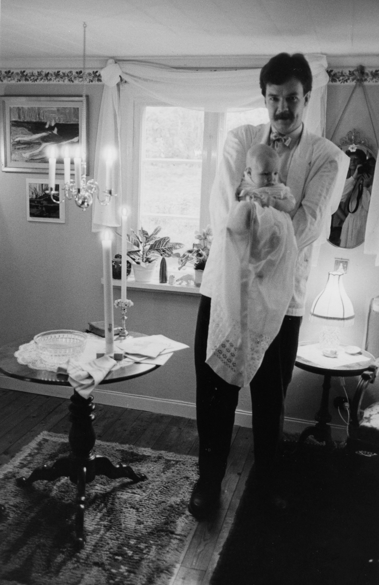 Manne Ekman (född 1955) håller dottern Emelie (född 1987) som är klädd i dopklänning, Vommedal Östergård "Petters" på Streteredsvägen 43, 1987-11-07.