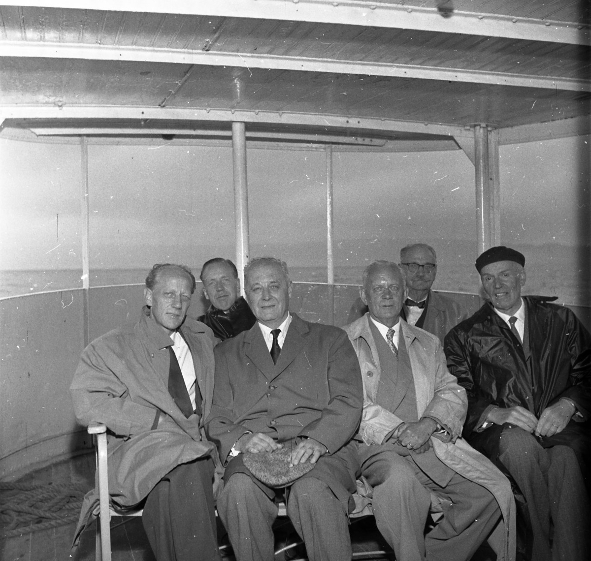 Sex herrar sitter i aktern på en båt. Alla ser in i kameran och ler. A E Bolling sitter längst bak till höger.

SJ Turisttrafik