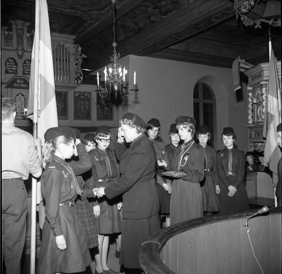 Scouter uppställda på led framför en scoutledare. De befinner sig i kyrkan. Ledaren gör honnör.