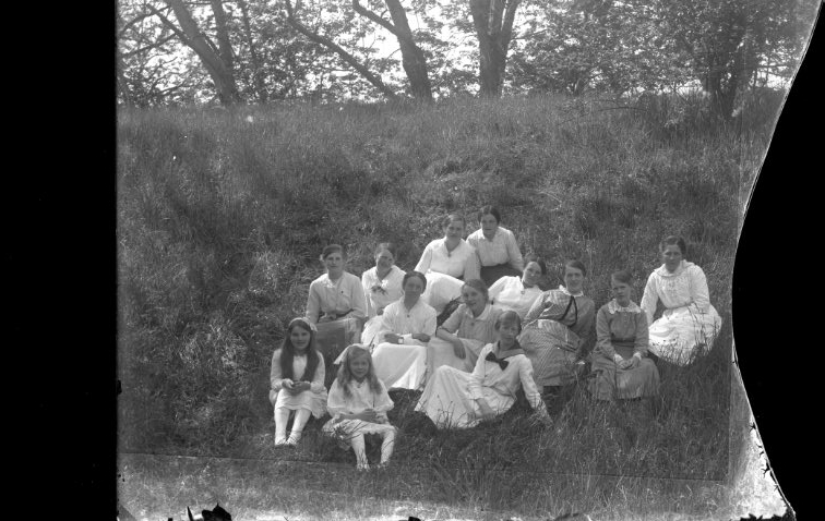 En grupp kvinnor och flickor sitter i en grässlänt. Det är sommar.