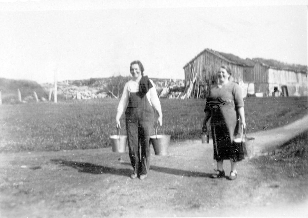 To personer på tur fra fjøset med melkespann i hendene. Ca1922.