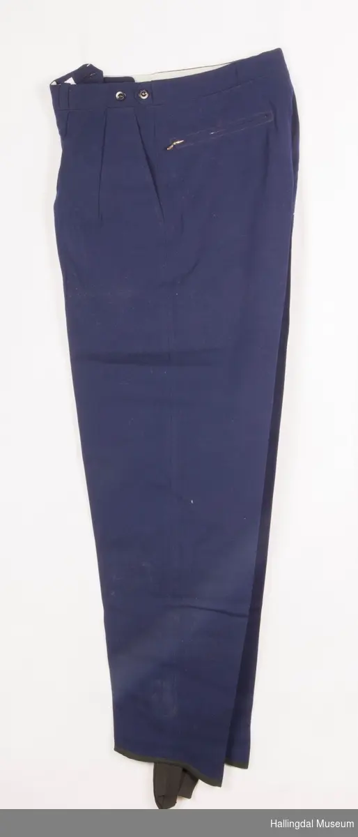 Mørk blå strekkbukse med knapper i gylfen, 2 lommer m/glidelås bak, 2 lommer framme.  2 legg framme.   Spensel inni linningen til stramming av livvidden.