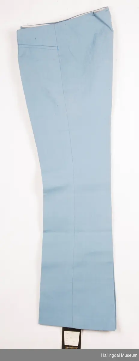 Lys blå bukse i bomull og polyester, slacks. Buksen er kort i livet.  Plastglidelås, 2 metallknapper.