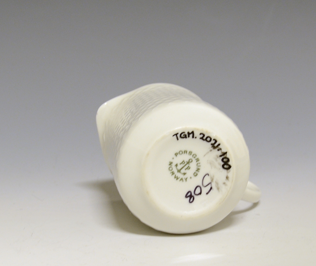 Fløtemugge av porselen med hvit glasur. Utvendig gitter i relieff, ørehank. 
Modell: 2380 Fasett