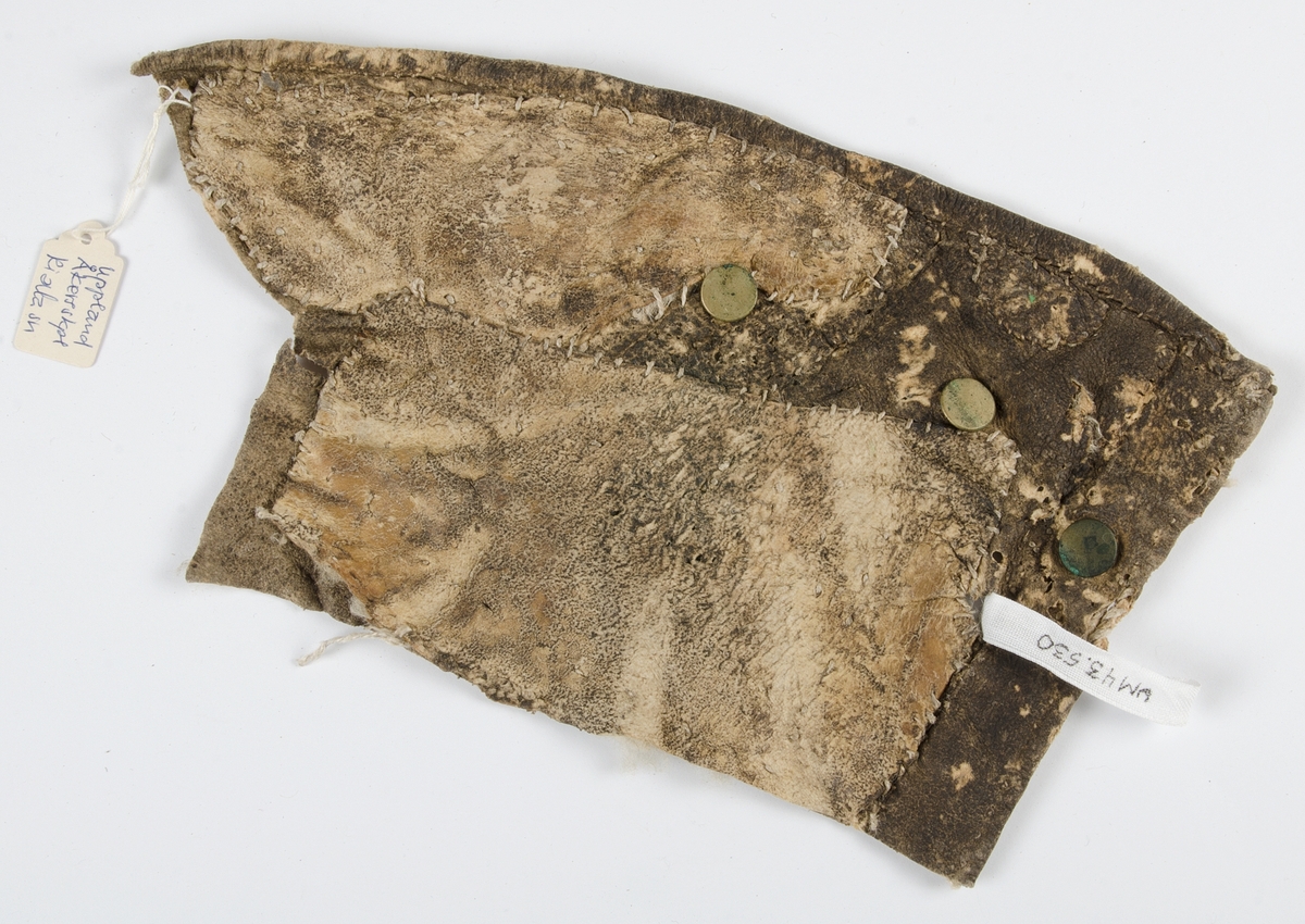 Fragment av pälsplagg med ullrester på insidan. Del av framstycke på tröja. Tre mässingsknappar med genomträdd skinnremsa på baktråden.