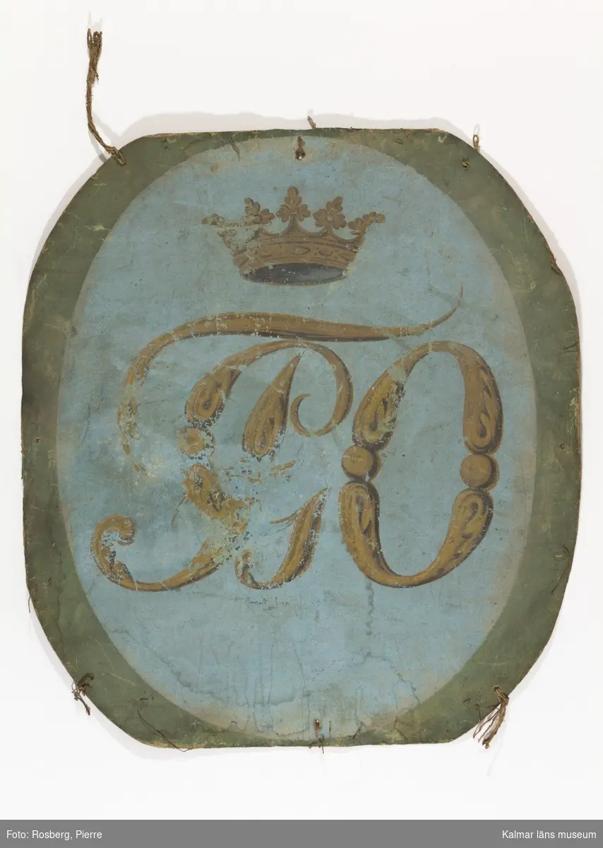 KLM 10612. Tavla, skylt. Oval papptalva målad med initialerna F G O under en gravkrona. Ordensattiralj eller festdekoration?