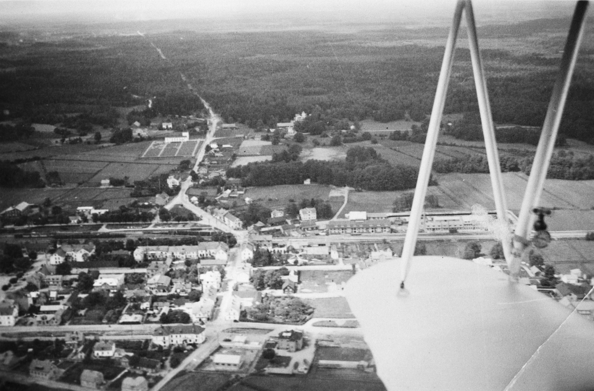 Flygbild av oidentifierat samhälle omkring 1930. Med flygplansvinge i förgrunden.