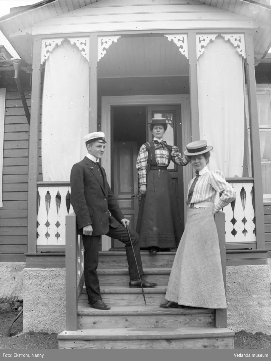 Två kvinnor och en man framför verandan till Nanny Ekströms fotoateljé på Kyrkogatan i Vetlanda. Kvinnan i mitten är fotografen själv.