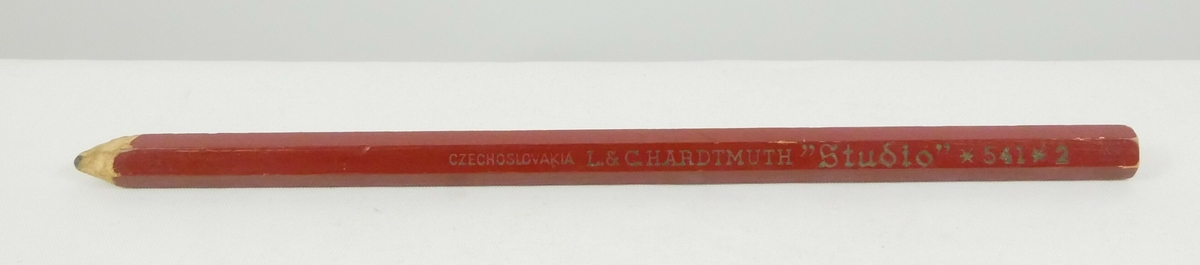 Rød blyant med harde kanter. Den er spisset i den ene enden. 