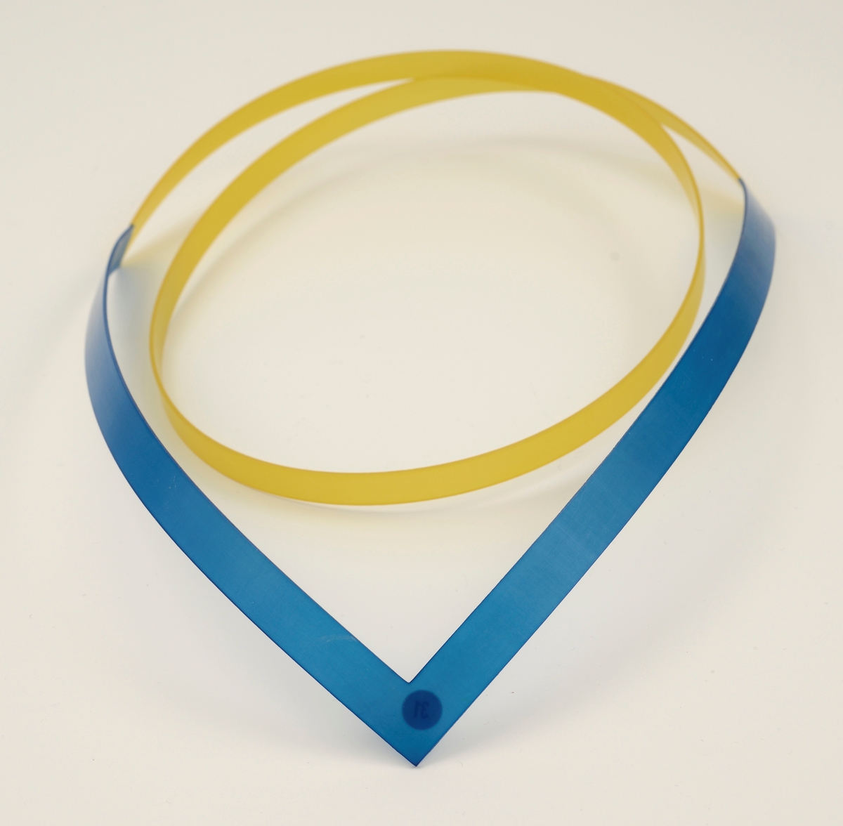 Halssmykke laget av stive nylonbånd som er cirka 1 cm brede. Foran er det et v-formet bånd i blå nylon, til dette er det festet et gult bånd som slynger seg i en spiral.