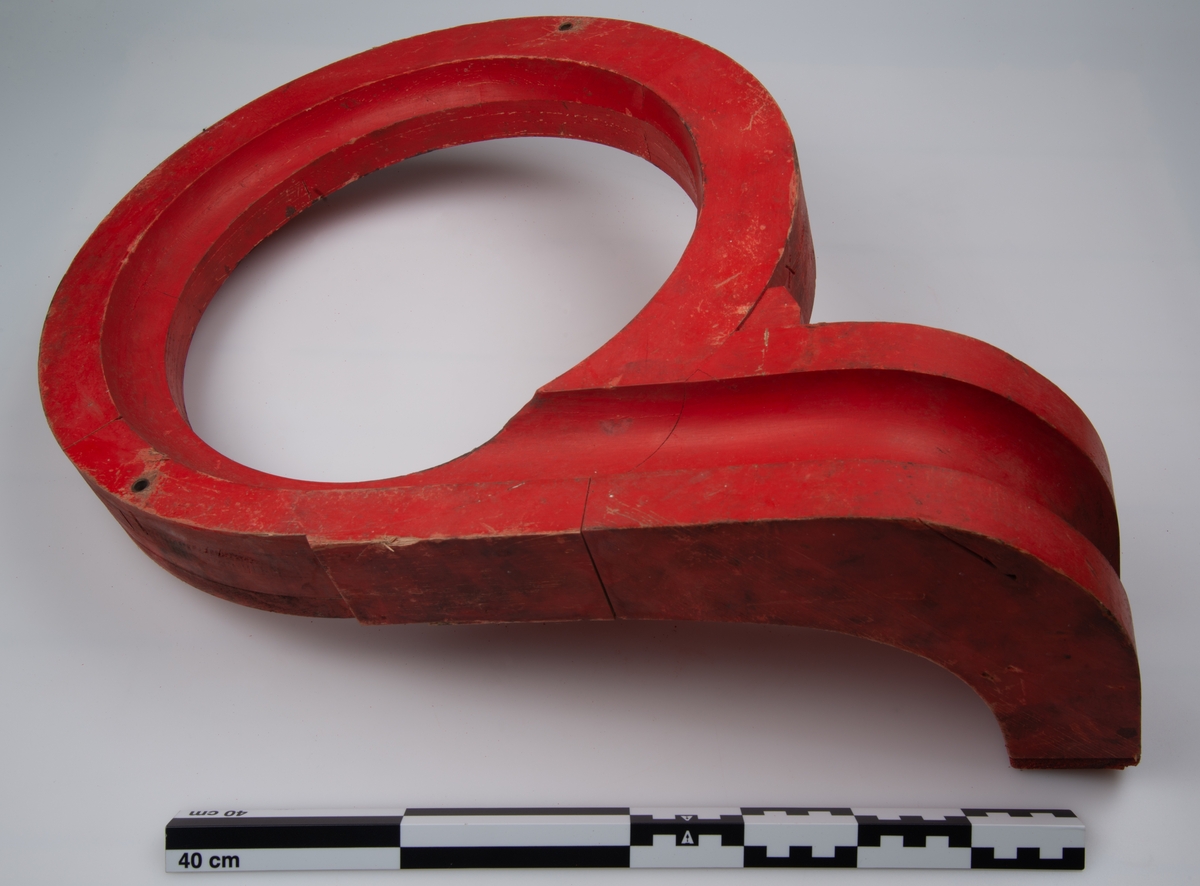Støpemodellen i tre er malt rød. den består av en ring som går ut i en tut. tuten i seg selv har en bøy som går 90 grader på ringen.  i denne tuten er det utsjært en kanal.