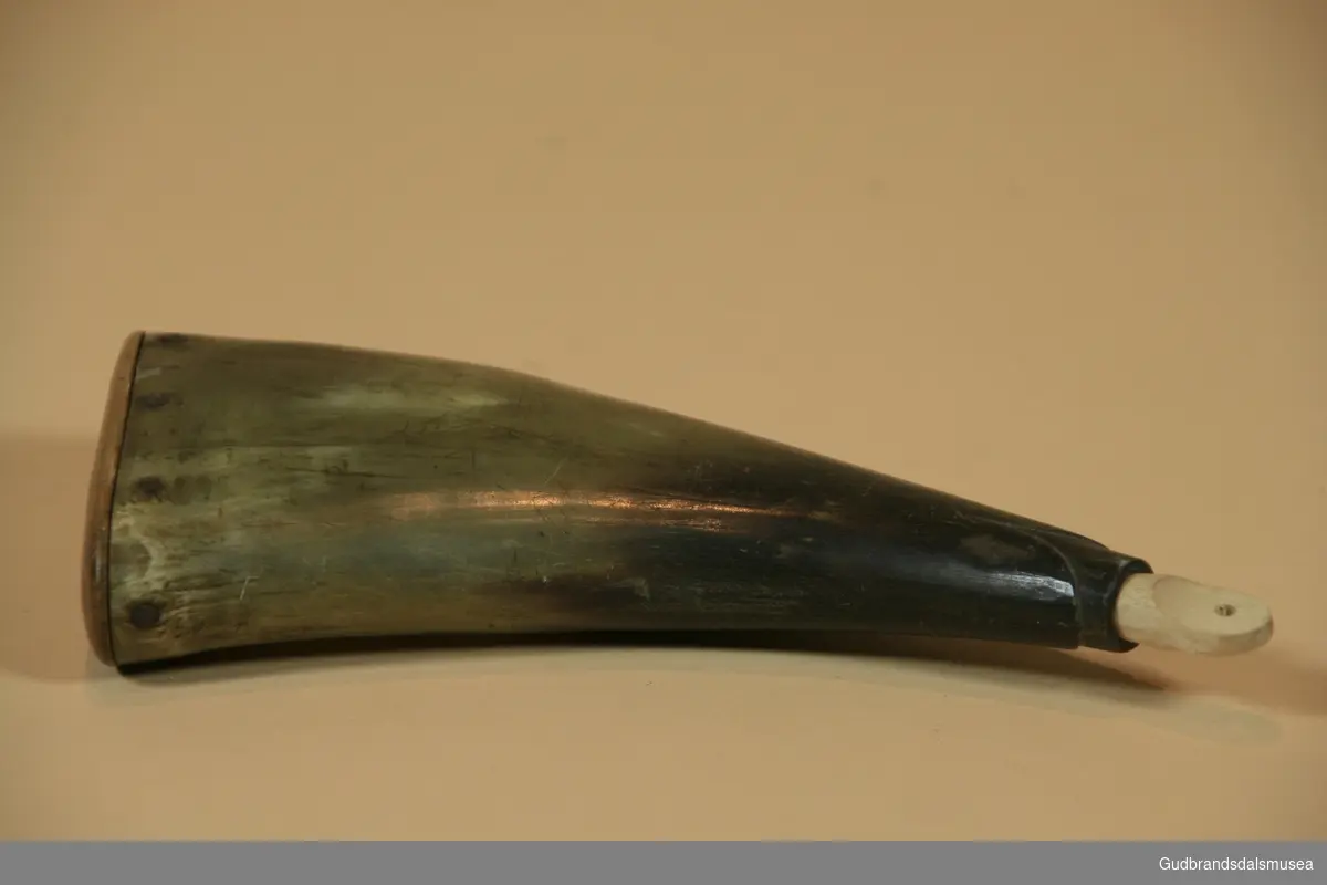Krutthorn i bein med trebunn festet med metallnagler. Tretapp i munning. Under ladning blir krutt tømt fra hornets spisse ende (munningen), der det kan være festet en måleinnretning.
