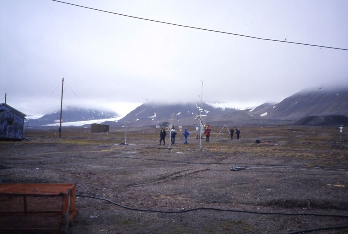 Ett turistsällskap bland olika mätinstrument. Höga berg och glaciär under låga moln i bakgrunden.