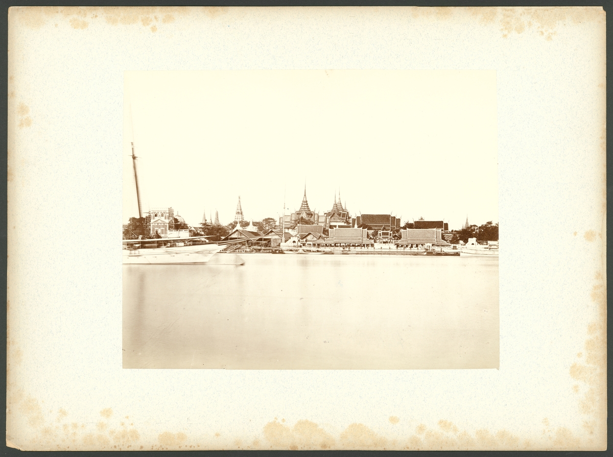 Bilden föreställer en historisk stadsvy över Bangkok med Chao Phraya​ floden och det kungliga palatset i centrum. På vänster sidan syns förskeppet av den kungliga ångjakten.