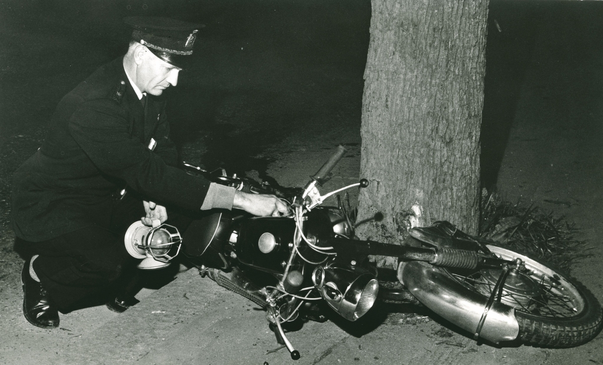 Politimann med motorsykkel som har kollidert i et tre.