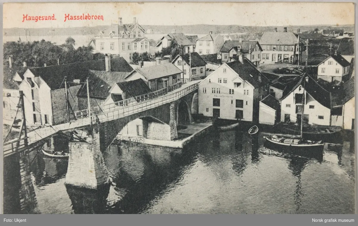 Postkort med bilde av broa over til Hasseløy i Haugesund sett fra fastlandssiden. Bygget til høyre for broa har påskriften "J. Hæstad Hummerforretning".