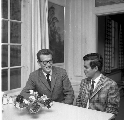 Rektorn för Grännaskolan, Sten Sarborn sitter och samtalar med en man. Båda klädda i slipsar. Framför dem på bordet står en bukett blommor.