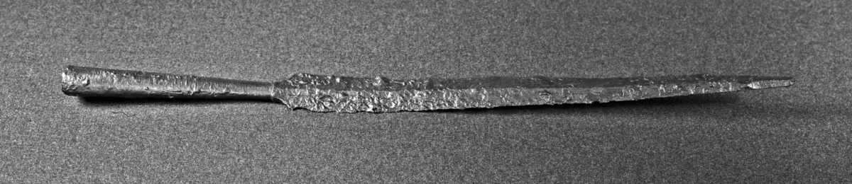 Spydspiss av jern, som Petersen: Vikingesverd fig. 21 eller Rygh 532. Dog er overgangen mellem fal og blad kortere og tverrere på dette eksemplar. Falen har vært ornert, visstnok med forskjellige mønstre, da der ennu vises tydelige horisontale graveringer i jernet. Den har og vært dekorert med sølvinnlegning, hvorav smeltede dråper sees. Lengde 58,5 cm. Bladets største bredde 3,8 cm