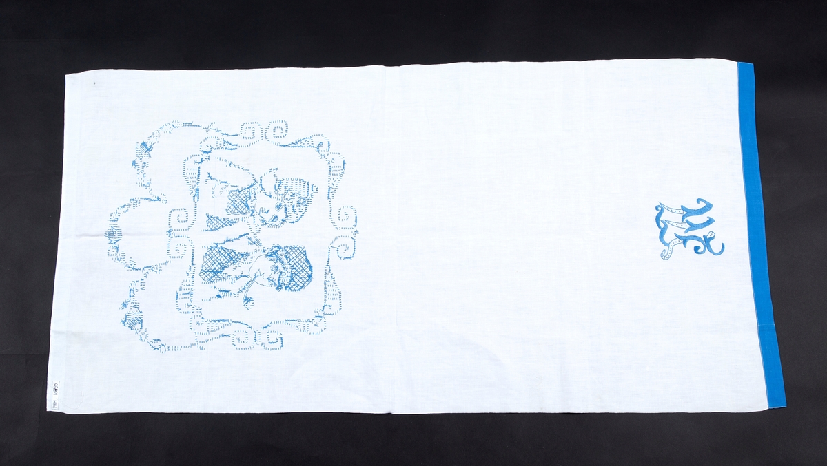 Pyntehåndkle, Hvit bunn, blå kanter. Brodert med en gutt og ei jente med korsting. Monogram M.

Gitt av Erna Madsen. Produsert av Margit Madsen.
Disse drev manufaktur i Drøbak.
