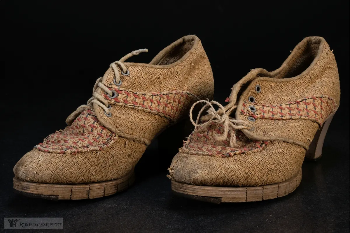 Høyhælte sko med tykk hæl og oppdelt såle i front. Sidene og fronten har partier med rødt og grått mønster.