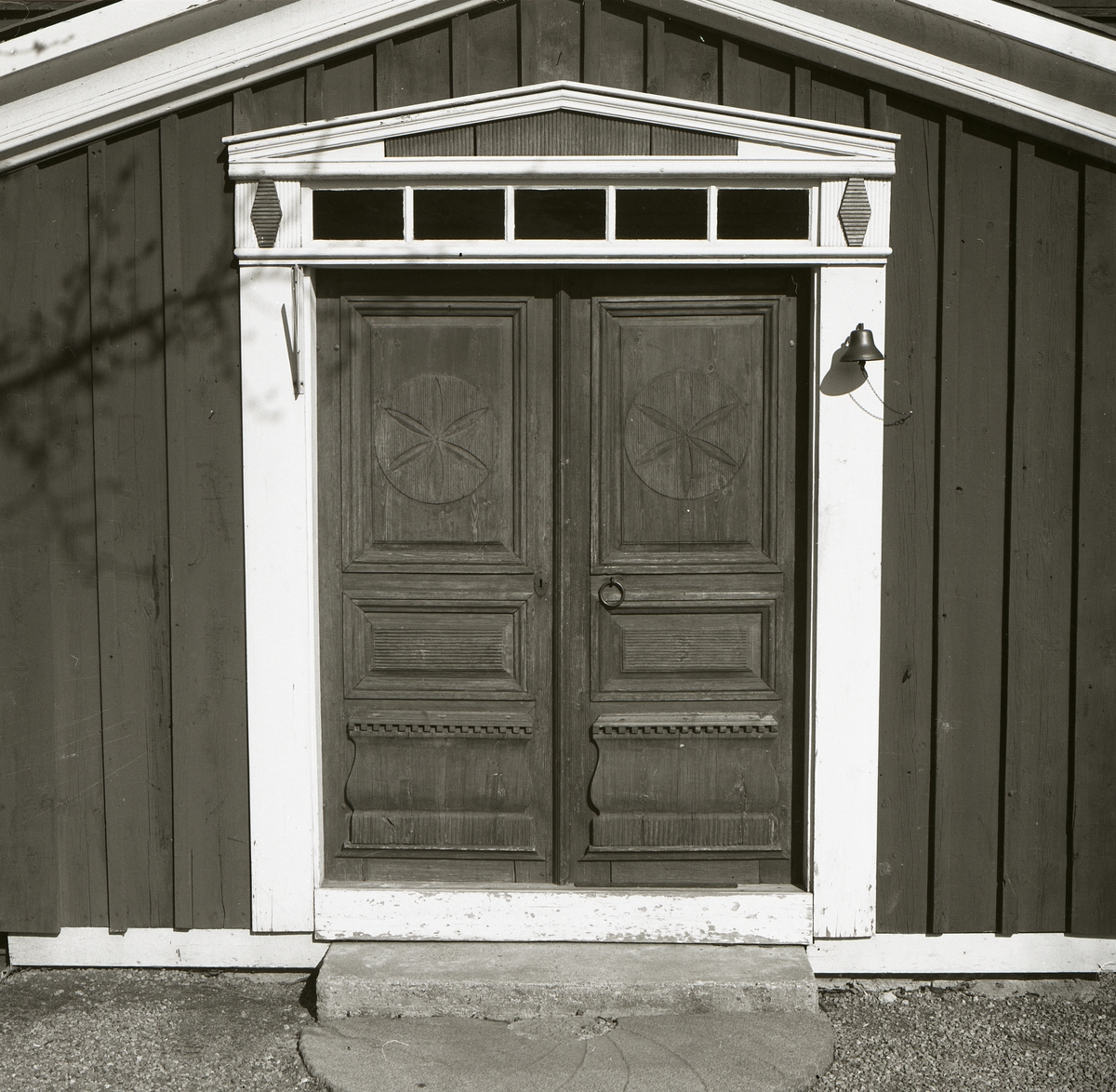 En inbyggd förstukvist med en pardörr med dörrspegel och fina sniderier.