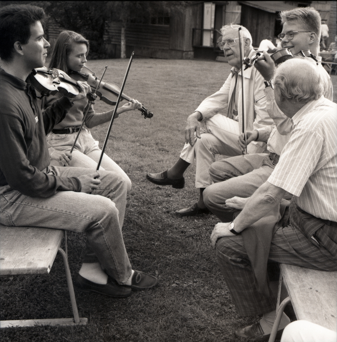 Tre ungdomar spelar fiol för två äldre män som sitter och lyssnar. 1992.