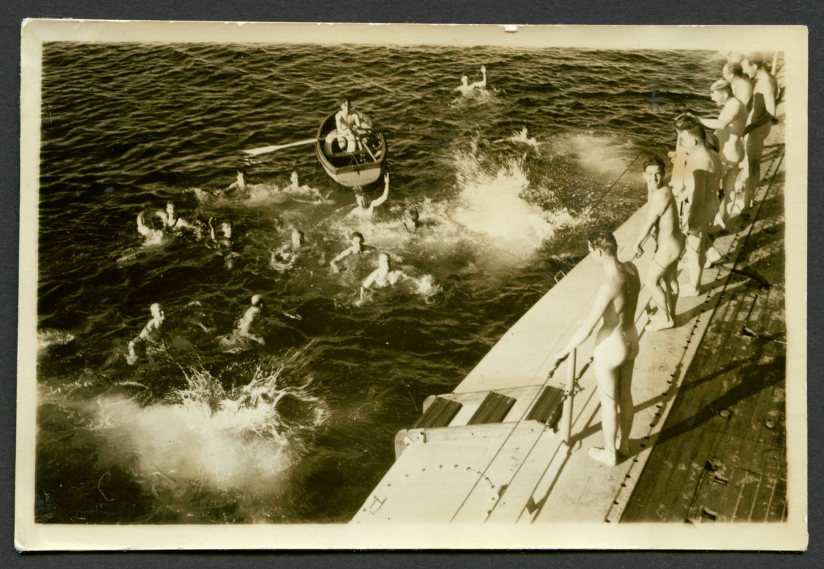 Bilden visar besättningen av en ubåt som badar i havet. En del av männen står avklädd på däcket.