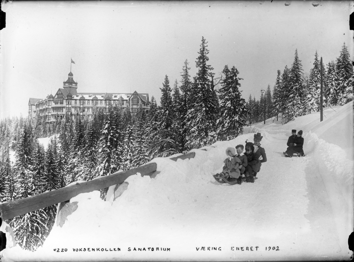 Voksenkollen sanatorium fotografert om vinteren med folk på kjelker i forgrunnen.