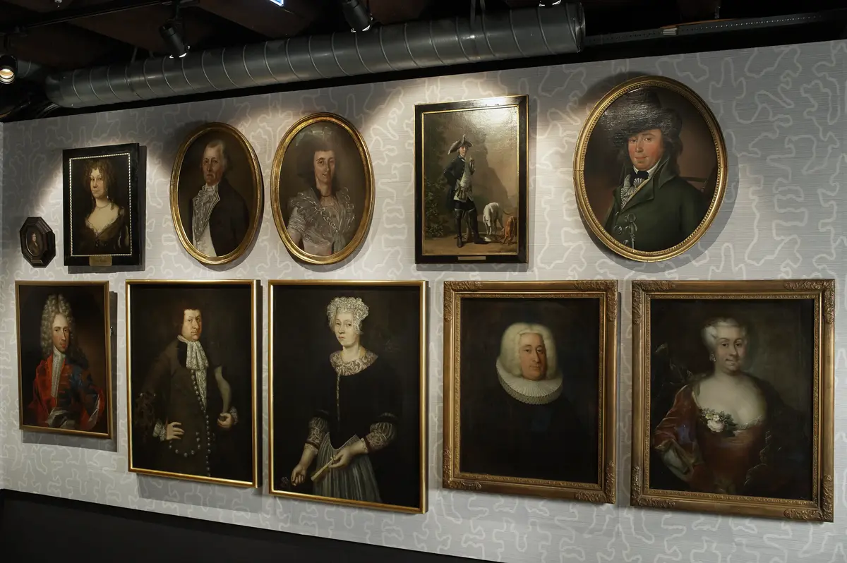 Fotografi av utstillingen OsLove ‒byhistorie for begynnere på Bymuseet i Oslo. Foto viser en utstillingsdel hvor vi ser flere portretter av velstående mennesker fra en tidligere tid.