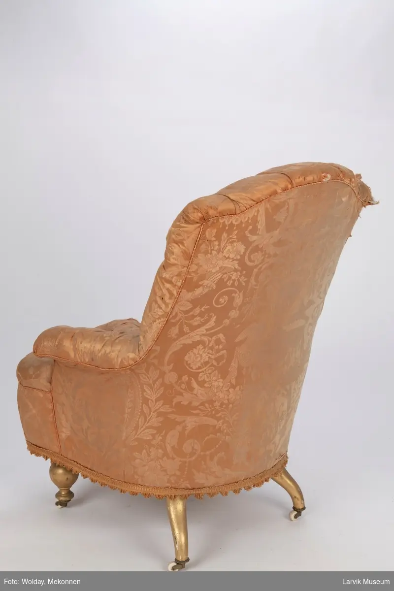 Lenestol med silketrekk, meget slitt. Gullmalte ben, hjul på benene i front på stolen.
