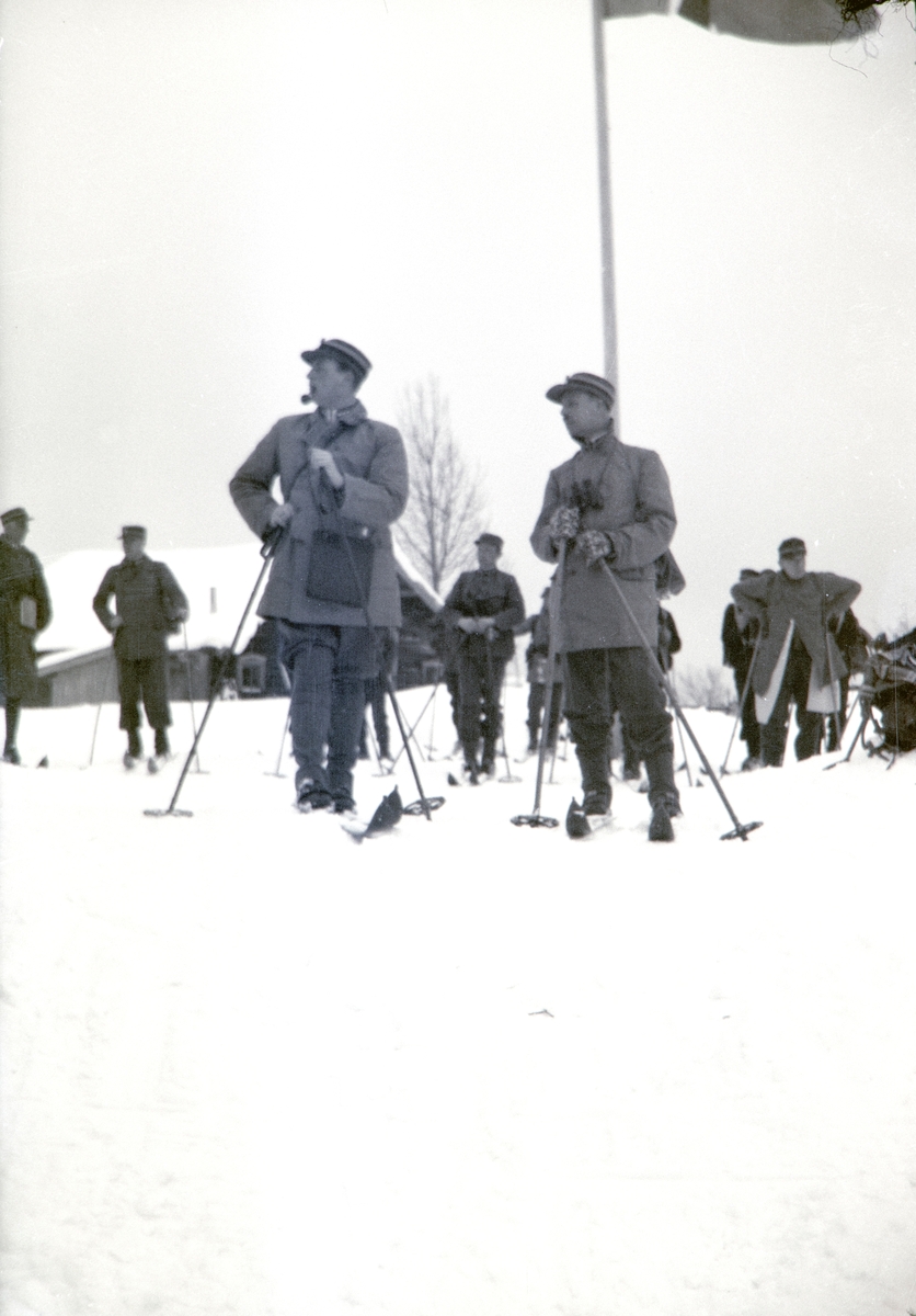 Militærøvelse i Romedal 1937. Vinterøvelse. Kronprins Olav stående på ski foran flaggstanga på Haukåsen. Vinter, snø, ski, militæret.