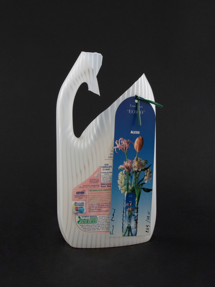 Vase laget av plastflaske for klesvaskmiddel. Kort med bilde av blomster i vase er festet til vasen med et grønt feste.
