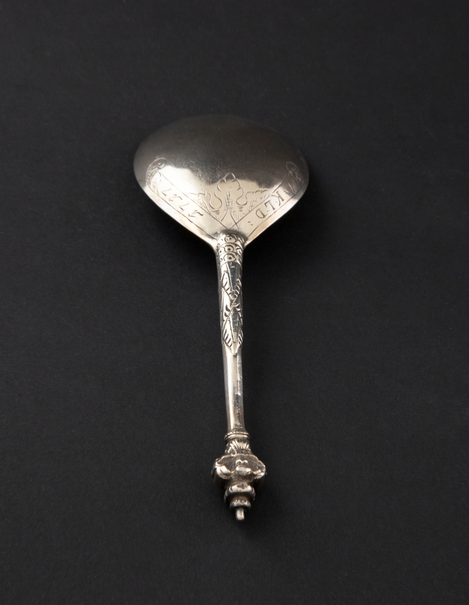 Kjerubskje i sølv med ornamentert skaft og dråpeformet skjeblad. Enden er dekorert med kjerubhoder på fremsiden og baksiden.