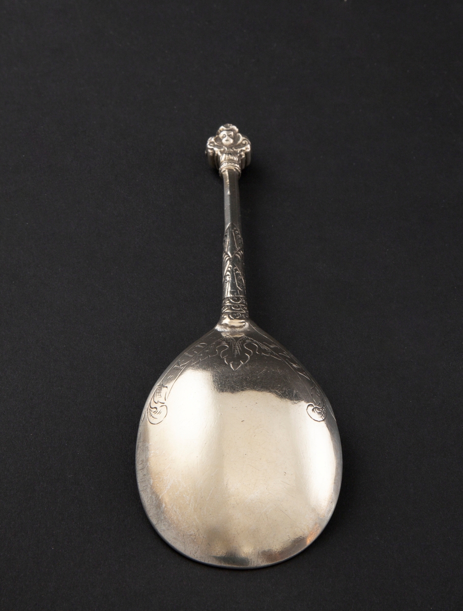 Kjerubskje i sølv med ornamentert skaft og dråpeformet skjeblad. Enden er dekorert med kjerubhoder på fremsiden og baksiden.