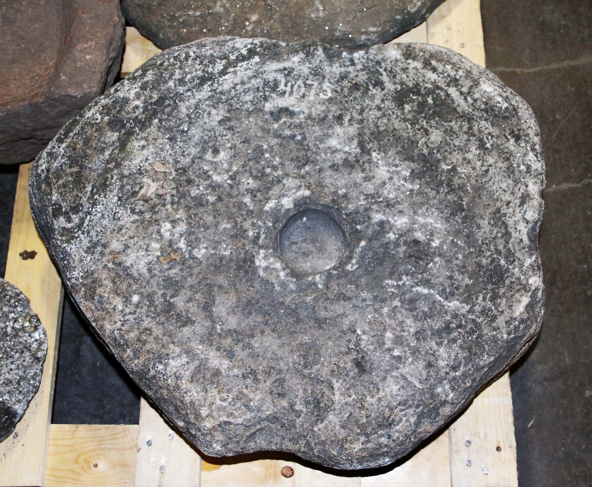 Liggare (understen) till handkvarn. Oregelbunden gråstenshäll, svagt konkav med rund fördjupning i mitten.

Funnen omkring år 1900 i en mad.