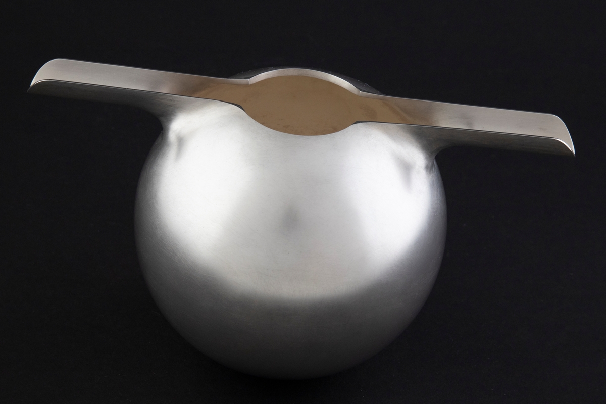 Tekanne for kald te i sølv, preget av et stramt geometrisk formspråk. Kuleformet korpus med to hanker, som også fungerer som tut, på hver side av den sirkulære munningen. Overflaten er mattet.