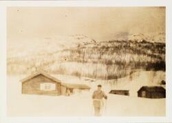 Påsken 1927 på Møsstrond. Mann på skitur, i bakgrunn laftet 