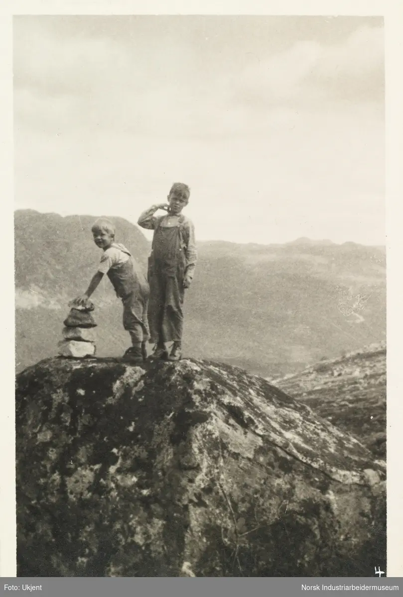 Over fjellet til Tomevatn på Møstrond. To gutter i snekkerbukse står på i fjellet ved en varde. I bakrunn fjellandskap