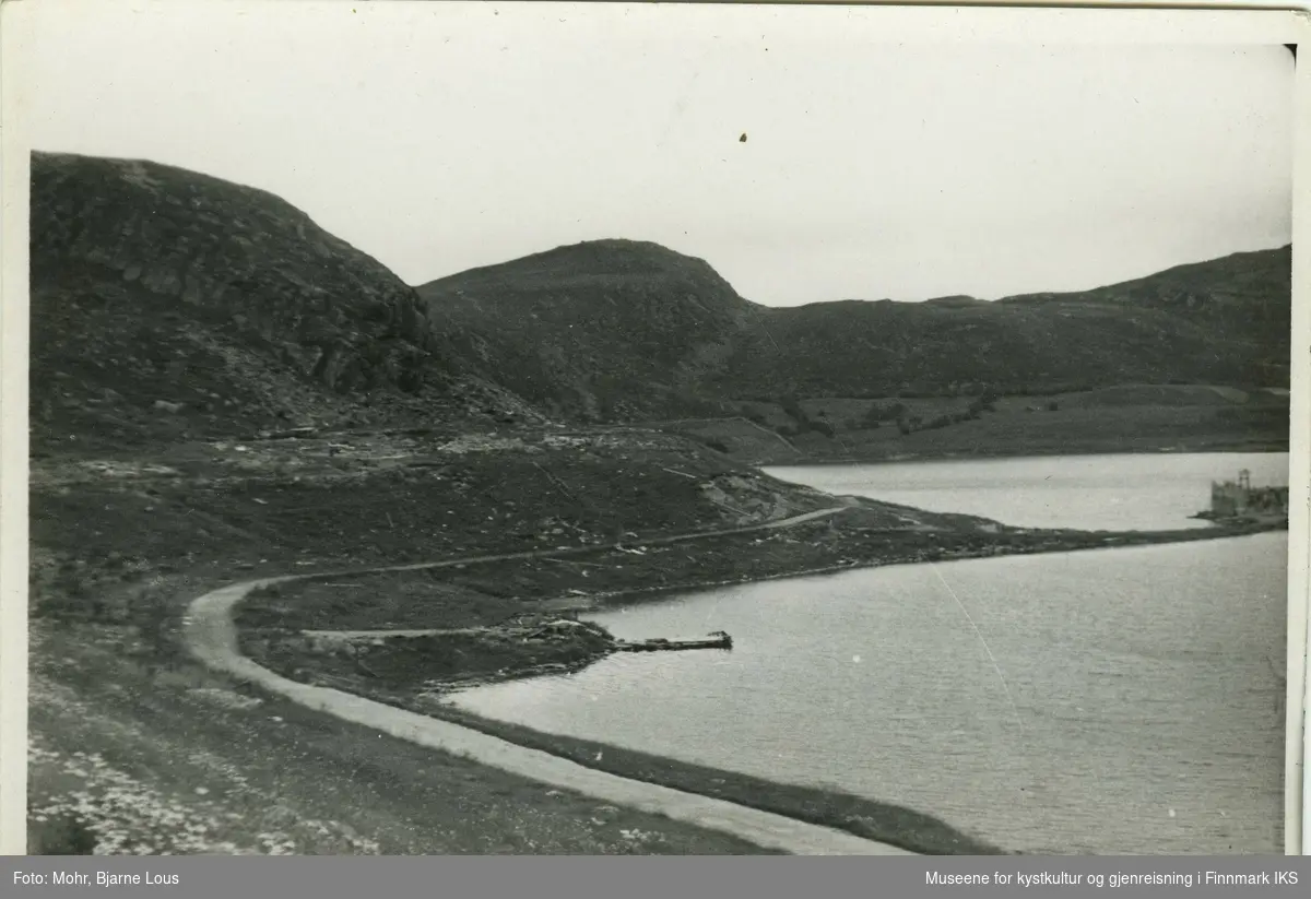 Breiliaområdet ved Storvannet i Hammerfest. Gata fører langs vannet. Man ser fjell i bakgrunn. På Holmen står det rester igjen etter noen byggning.