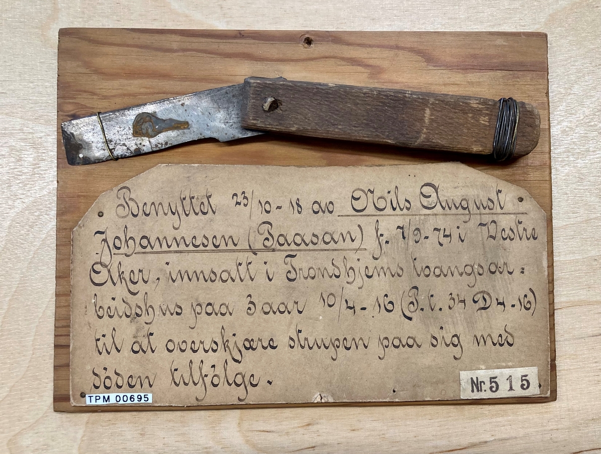 Hjemmelaget kniv med brukket blad, montert på treplate sammen med en papirlapp med håndskrevet tekst.