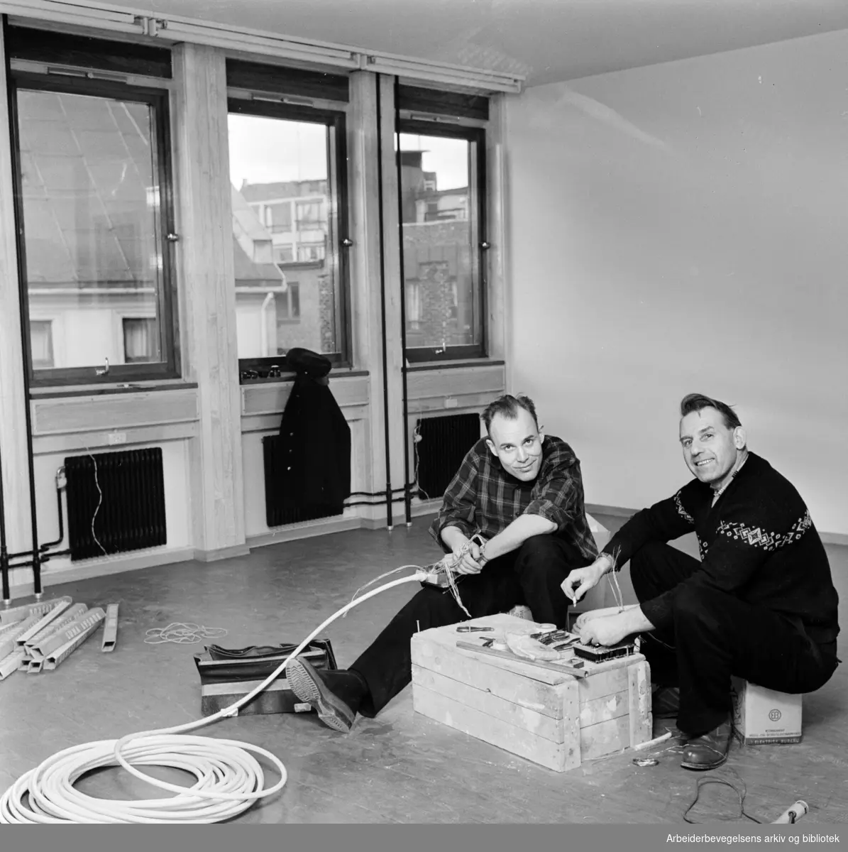 Telefonmontørene Svein Isachsen og Gunnar Gulbrandsen gjør klar telefonlinjene i det nye Folkets Hus på Youngstorget. Februar 1962.
