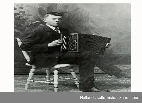 Johannes Gunnarsson (Sjöland) från Normans-torp, Gällared. Rallare och skicklig dragspelare . Fotograferad 1910 med sitt dragspel. Sitter på en vacker stol.
