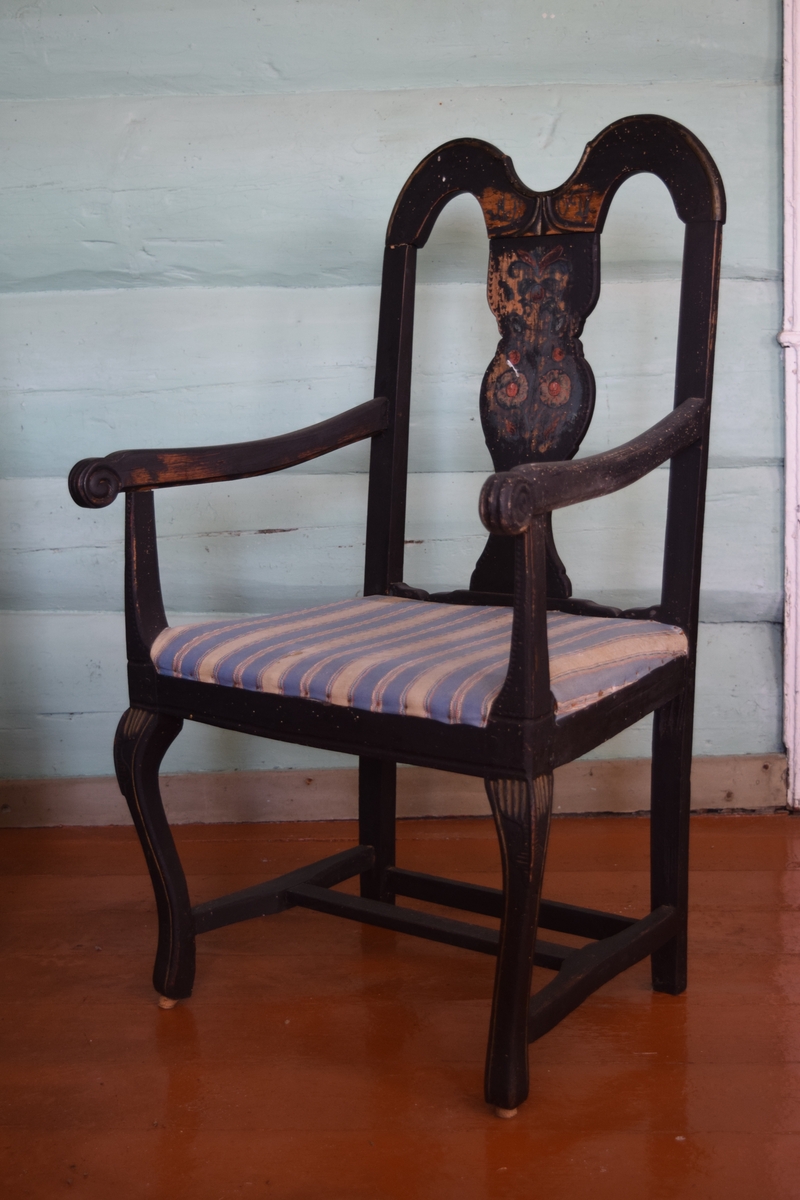 Sortmalt stol i tilnærmet rokokkostil (1700-årene) - bonderokoko. Midtfeltet i ryggen har blomsterdekor og initialer. Trekket er hjemmevevd i en blåfarge.