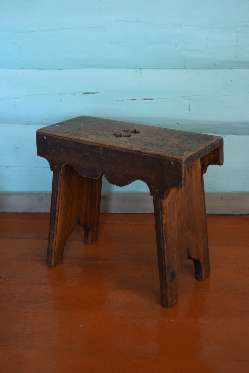 Høybent krakk av furu. 1700-talls. Krakken har to ben laget av to vertikalt stående bordbiter. Sidene på krakken er utskåret i tungemønster. Selve setet har to hjerter som dekorasjon.
