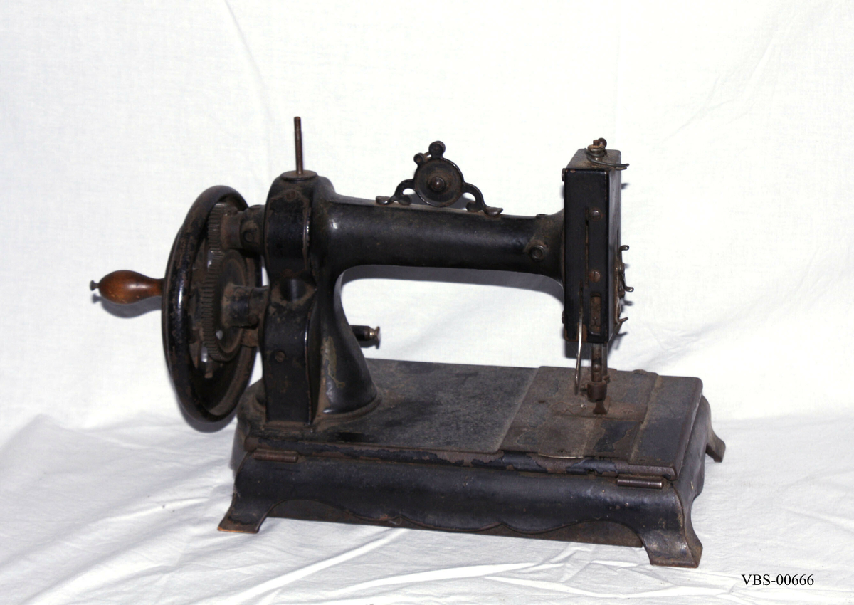 Symaskin med sveiv i svart jern. Den er festet med to hensgler på en solid sokkel av 6 cm i støpejern.   
Muligens produsert av GROVEN & BAKER (Boston, USA), produsenter siden 1851.